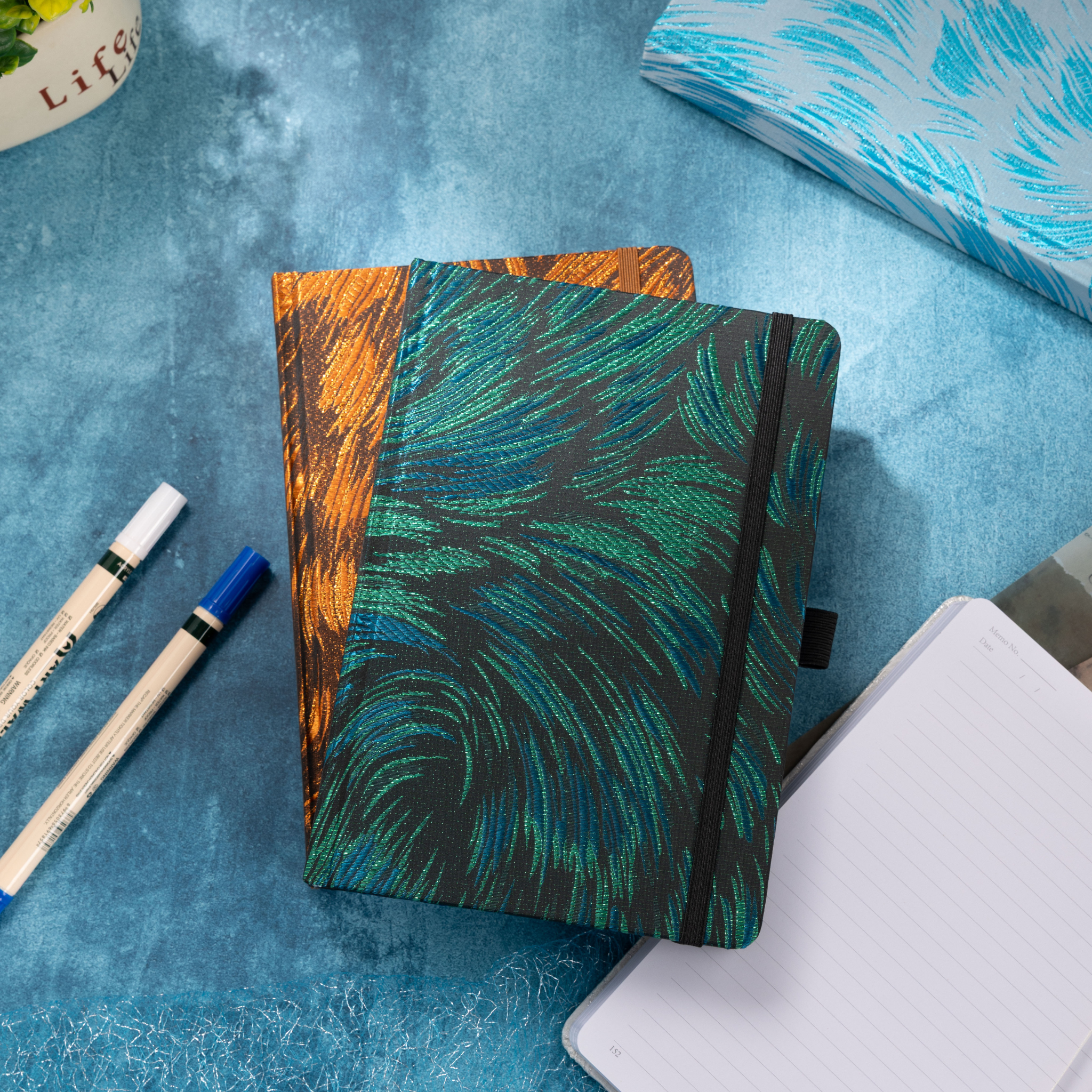Open 100gsm lined paper page partially visible underneath a textured green embroidered journal, showing the paper choices available with fabric cover notebooks.