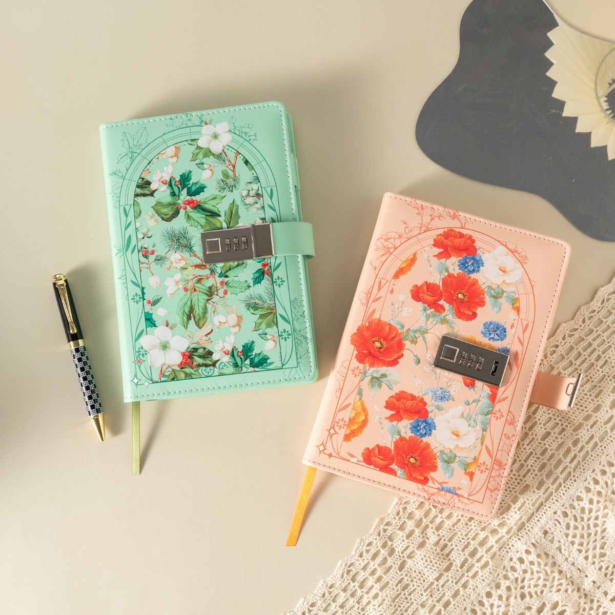 Two floral notebooks, one mint green and one orange, with combination-lock clasps beside a pen.
