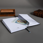 Inner back pocket of the Dream Garden lily notebook holding a color illustrated card, with a blue ribbon bookmark visible, styled with books on a dark wooden surface.