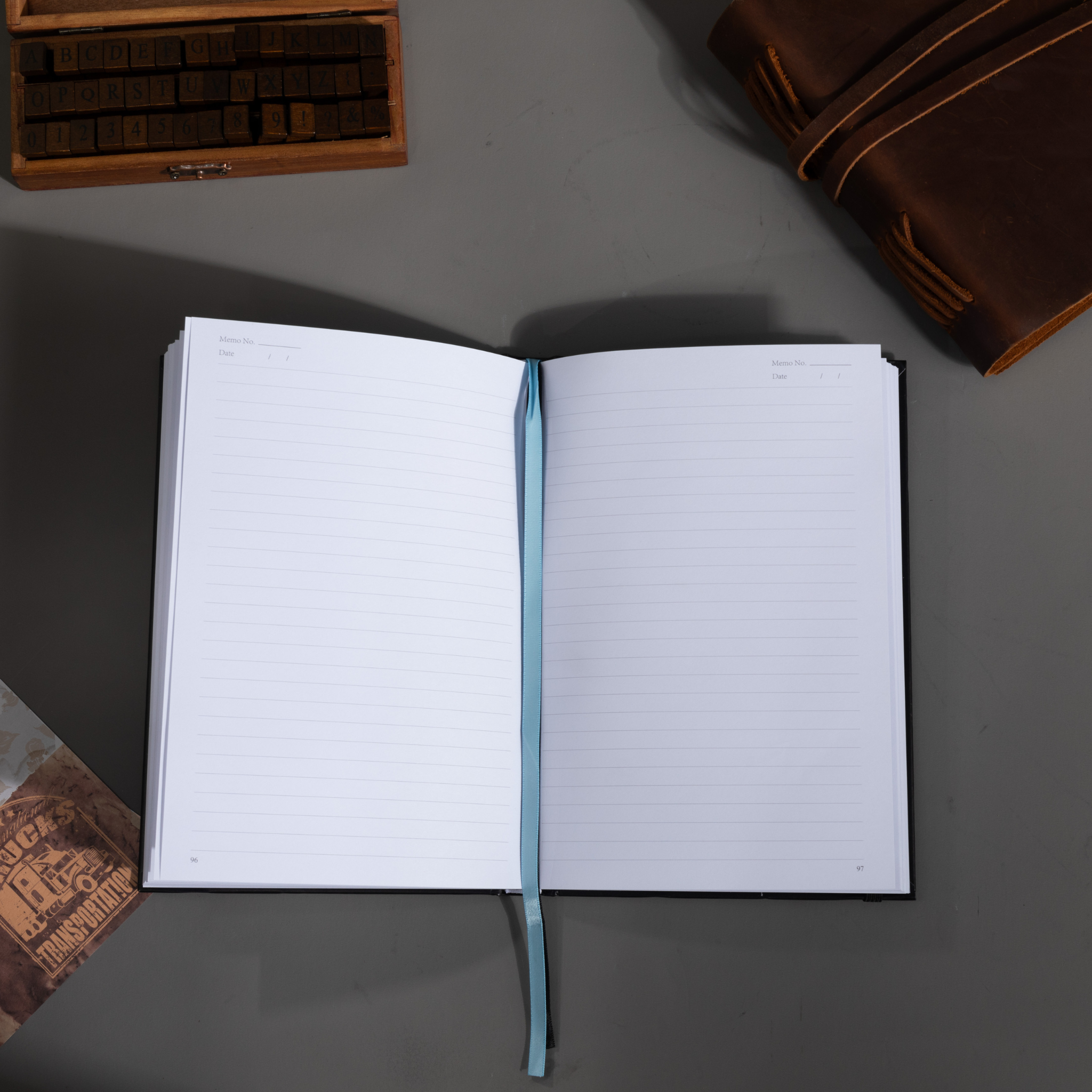 Open A5 lined notebook showing clean white pages with Date and Memo No. headers, a blue ribbon bookmark, and a black elastic closure.