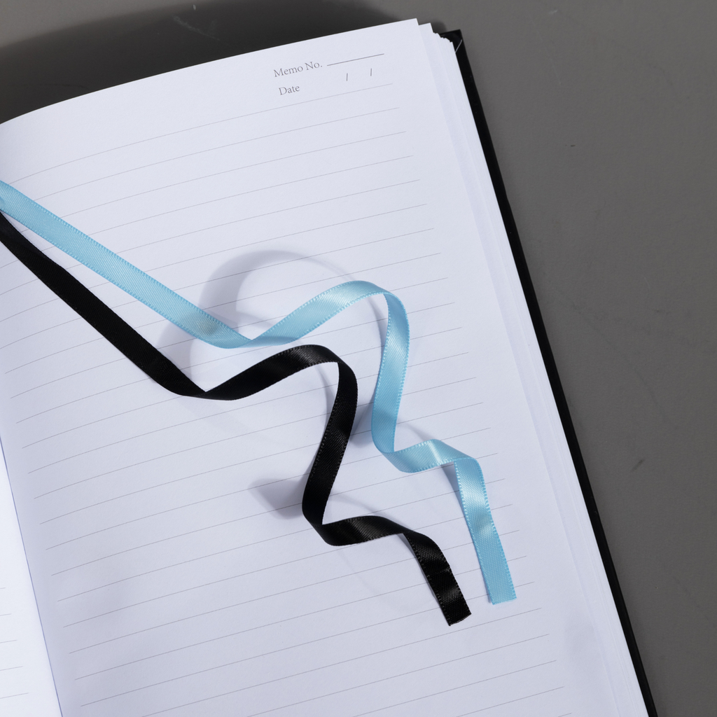 Close-up of the black and blue two-tone ribbon bookmark resting elegantly on the open lined pages of the lily Dream Garden notebook.