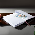 Inner back pocket of the Dream Garden notebook holding a color illustrated card, with a pink ribbon bookmark visible, styled on a dark reflective surface.