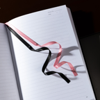 Close-up of the black and pink two-tone ribbon bookmark resting elegantly on the open lined pages of the Dream Garden notebook.