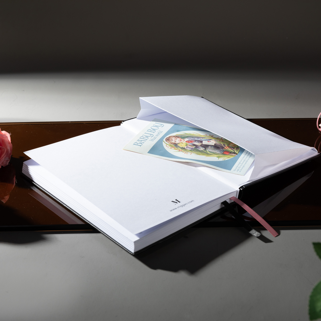 Inner back pocket of the Dream Garden notebook holding a color illustrated card, with a pink ribbon bookmark visible, styled on a dark reflective surface.