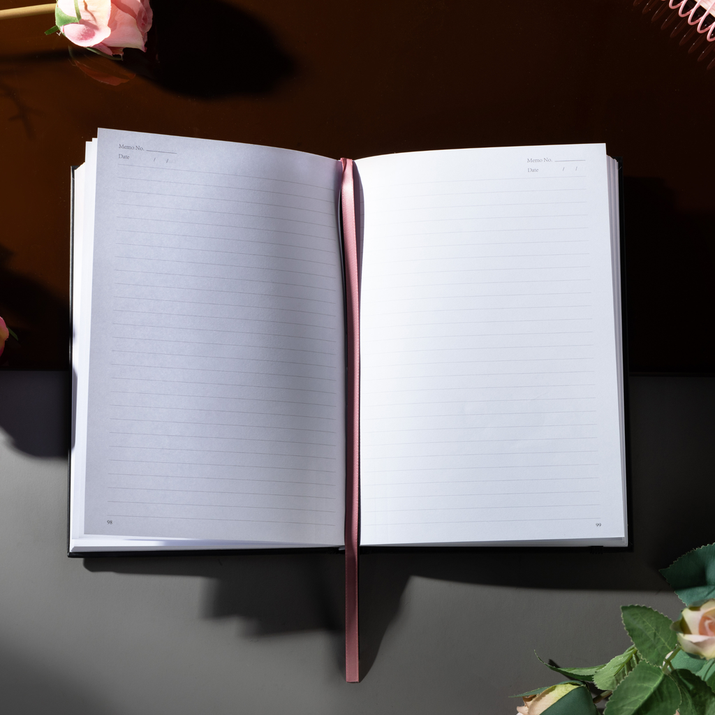 Open A5 lined notebook showing clean white pages with Date and Memo No. headers, a pink ribbon bookmark, and a black elastic closure.