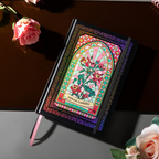 Angled flat lay of the black and pink holographic Dream Garden cardboard notebook resting on a dark reflective surface, featuring a vibrant floral arch design with holographic neon accents, and styled with fresh pink roses.