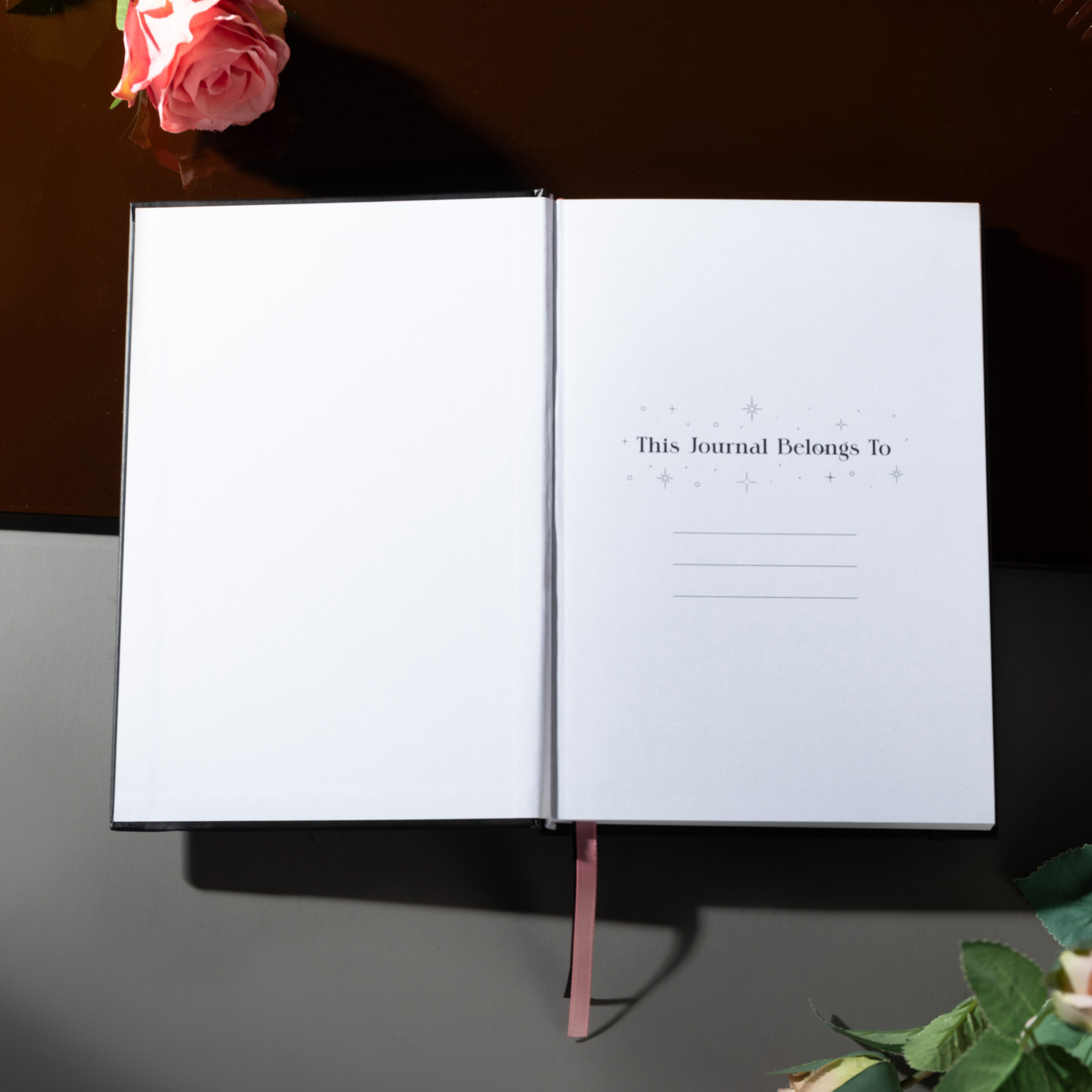 Open Dream Garden notebook showing the "This Journal Belongs To" ownership page with delicate star and circle details, styled with pink roses on a dark surface.