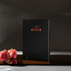 Back cover of the black Dream Garden cardboard notebook standing upright, featuring a minimalist "DREAM GARDEN" logo and star design, styled with pink roses.