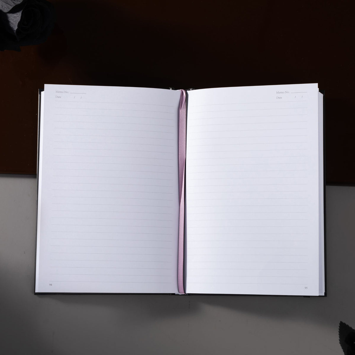Open A5 lined notebook showing clean white pages with Date and Memo No. headers, a pink ribbon bookmark, and a black elastic closure.