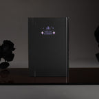 Back cover of the black Dream Garden cardboard notebook standing upright, featuring a minimalist "DREAM GARDEN" logo and star design on a dark surface.