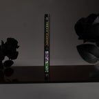 Spine view of the black iris Dream Garden cardboard notebook standing upright on a dark surface, featuring the holographic "DREAM GARDEN" title and geometric details.