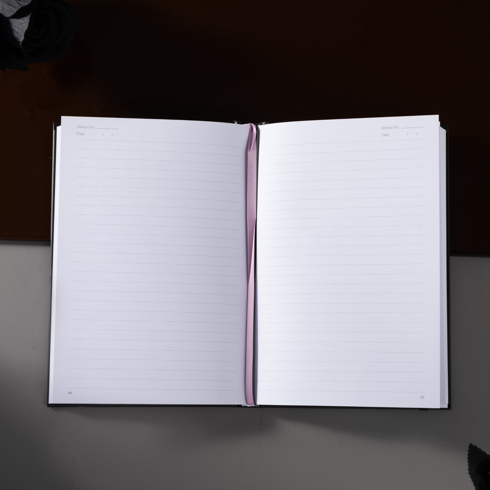 Open A5 lined notebook showing clean white pages with Date and Memo No. headers, a pink ribbon bookmark, and a black elastic closure.