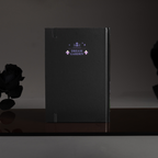 Back cover of the black Dream Garden cardboard notebook standing upright, featuring a minimalist "DREAM GARDEN" logo and star design on a dark surface.