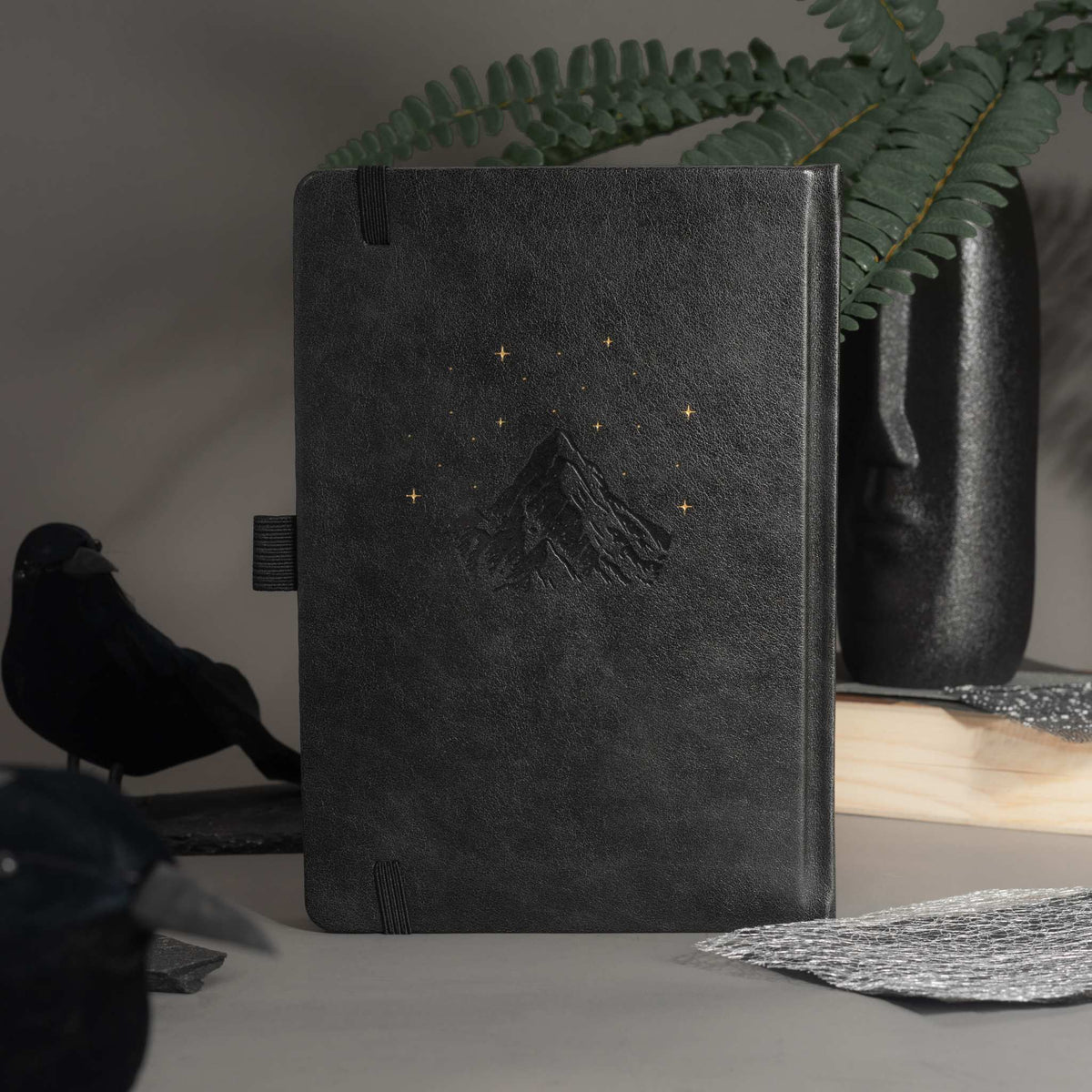 Elegant back cover of the black vegan leather notebook featuring embossed gold foil stars and moon, styled on a moody desk setup.