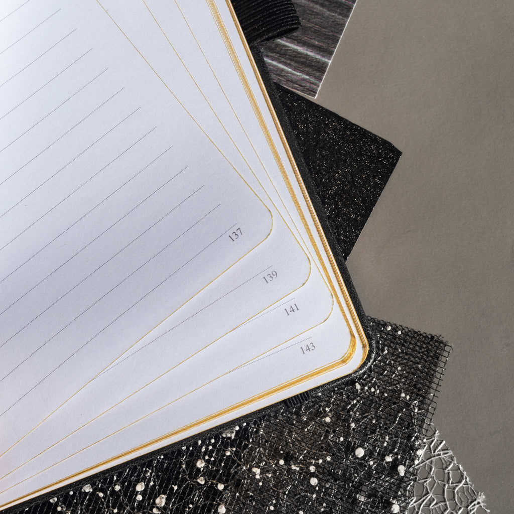 Close-up of the open A5 notebook showing the 100gsm lined paper interior with golden borders and corner. 