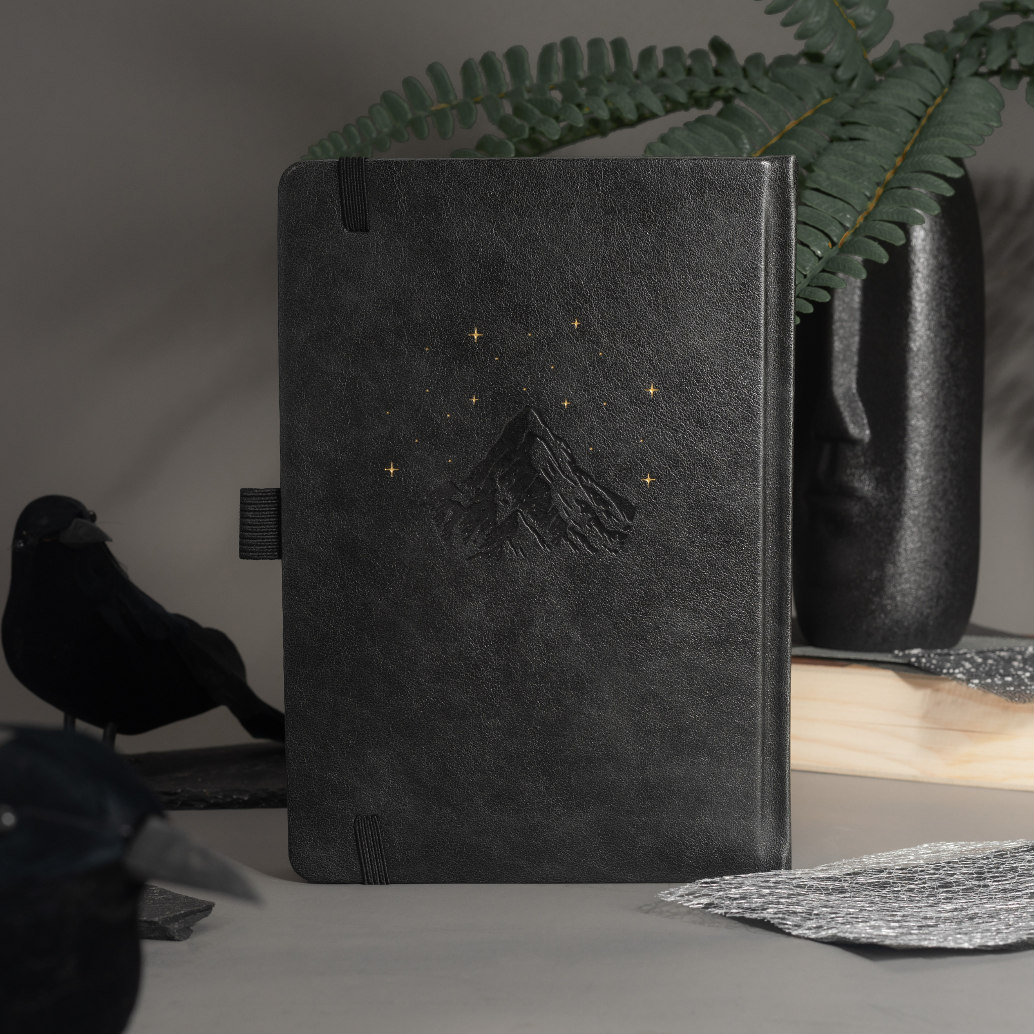 Elegant back cover of the black vegan leather notebook featuring embossed gold foil stars and moon, styled on a moody desk setup.