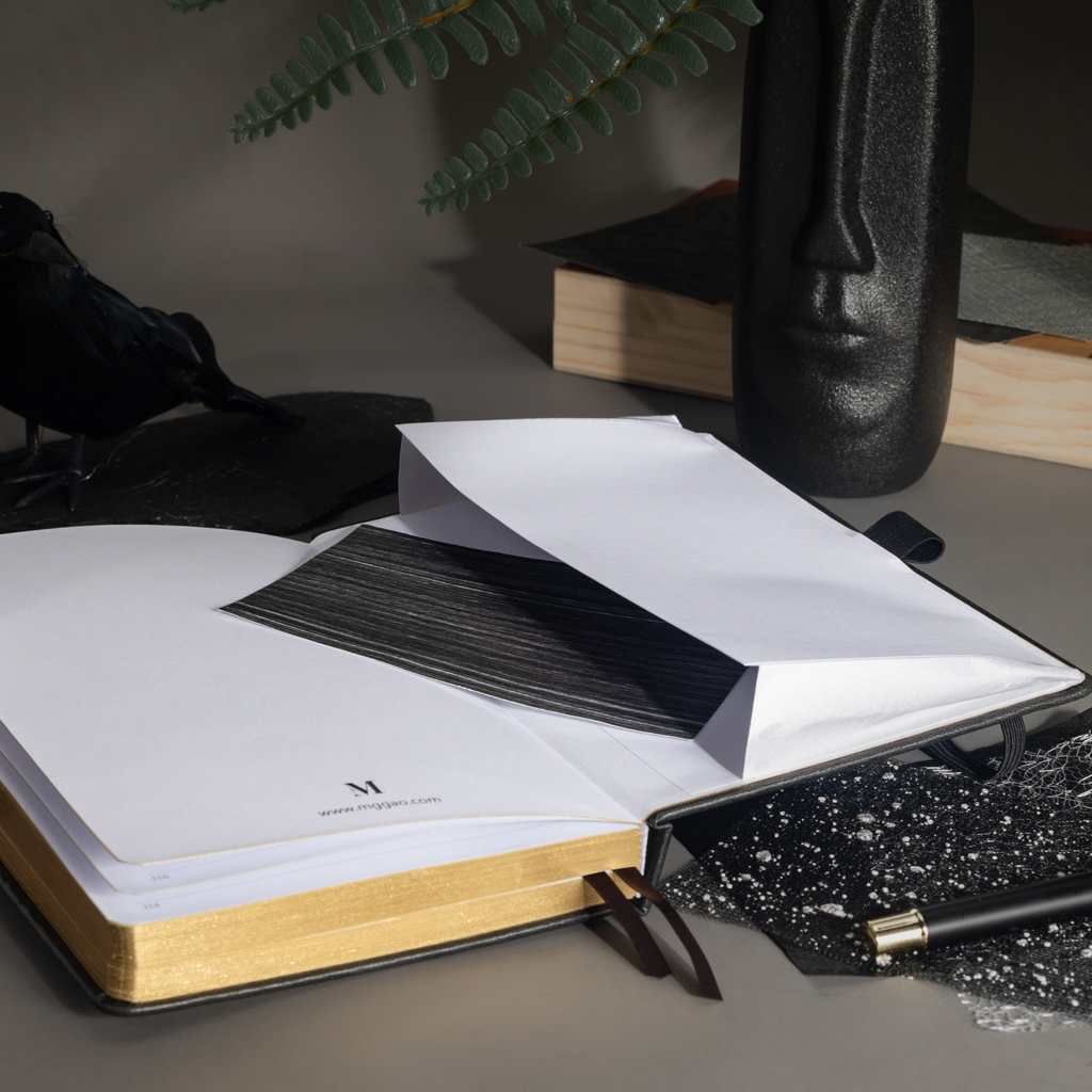 Inner back pocket of the black vegan leather notebook holding a dark patterned card, with gold gilded edges visible at the bottom.