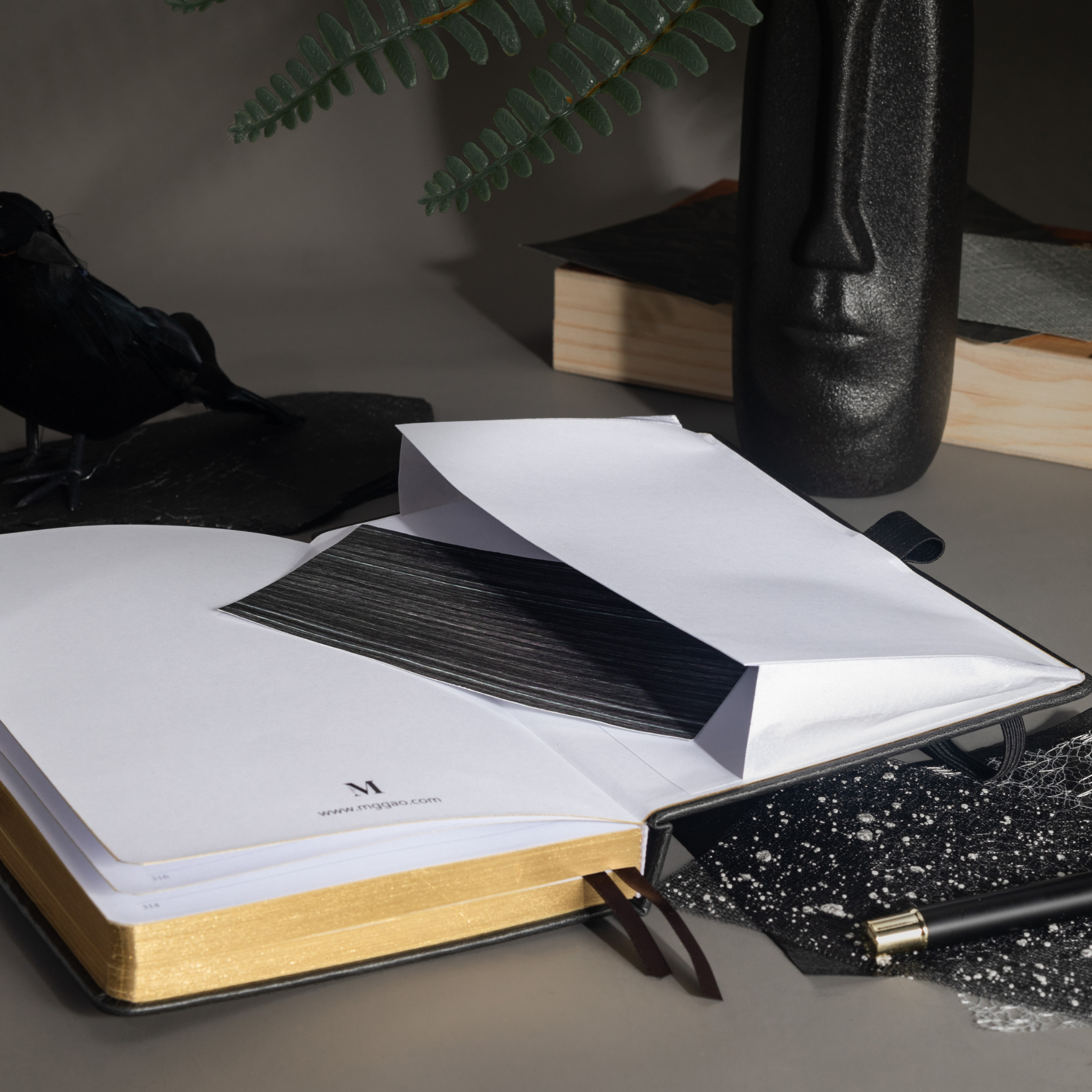 Inner back pocket of the black vegan leather notebook holding a dark patterned card, with gold gilded edges visible at the bottom.