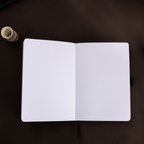 Open A5 journal laid flat on a dark surface, displaying the clean 160gsm dot grid paper interior and a black ribbon bookmark.
