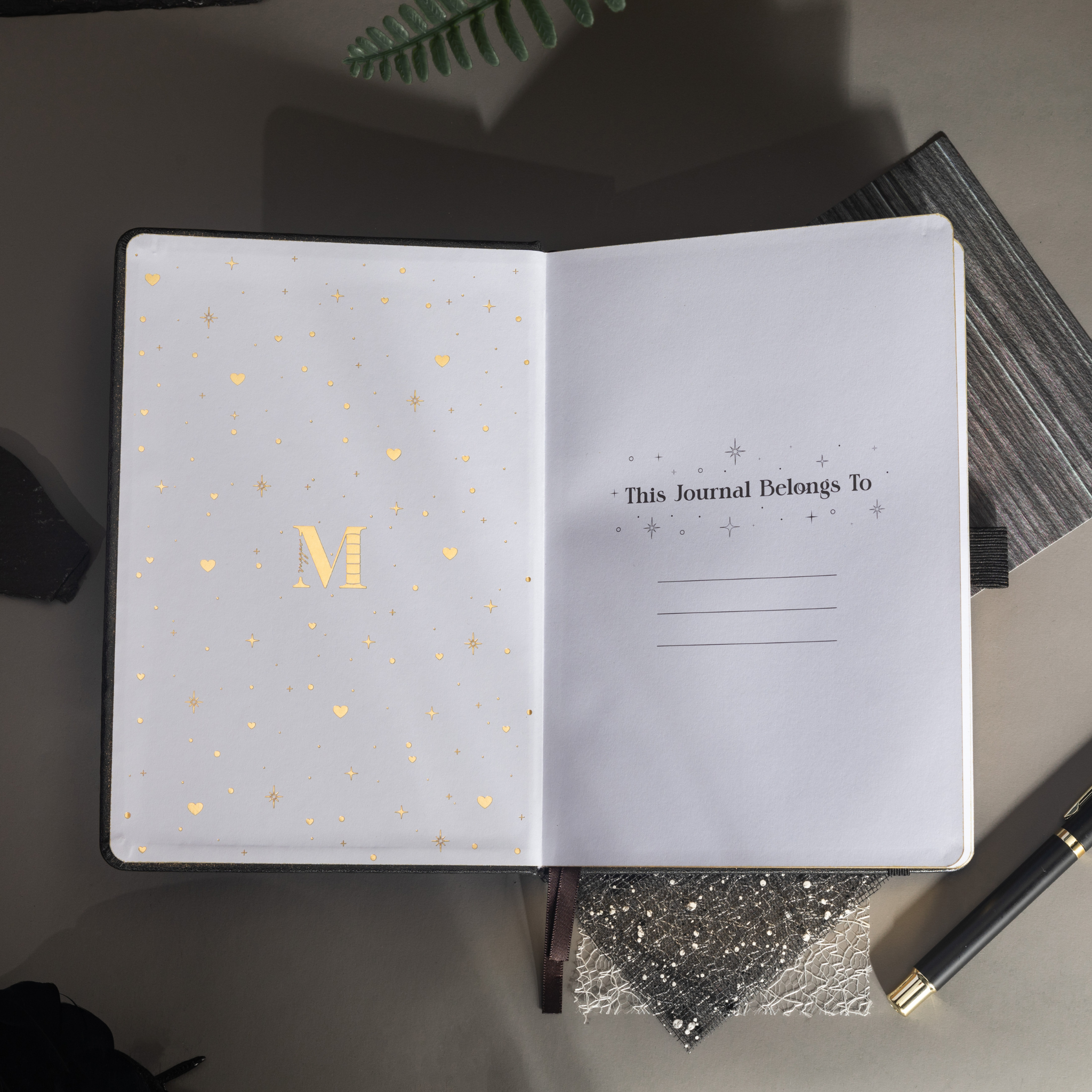 Inside opening page of the black mountain journal featuring a gold foil "M" logo and "This Journal Belongs To" ownership section.