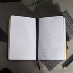 Open A5 notebook lying flat, showing the 100gsm lined paper interior with a black ribbon bookmark and black side pen loop.