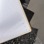 Close-up of the open A5 notebook showing the 100gsm lined paper interior with golden borders and corner numbers.