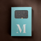 Light blue window-cut gift box featuring a white "M" logo, displaying the black mountain vegan leather notebook inside.