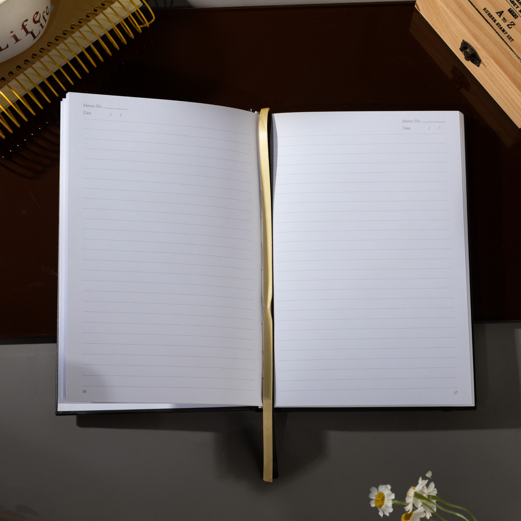 Open A5 lined notebook showing clean white pages with Date and Memo No. headers, a gold ribbon bookmark, and a black elastic closure.