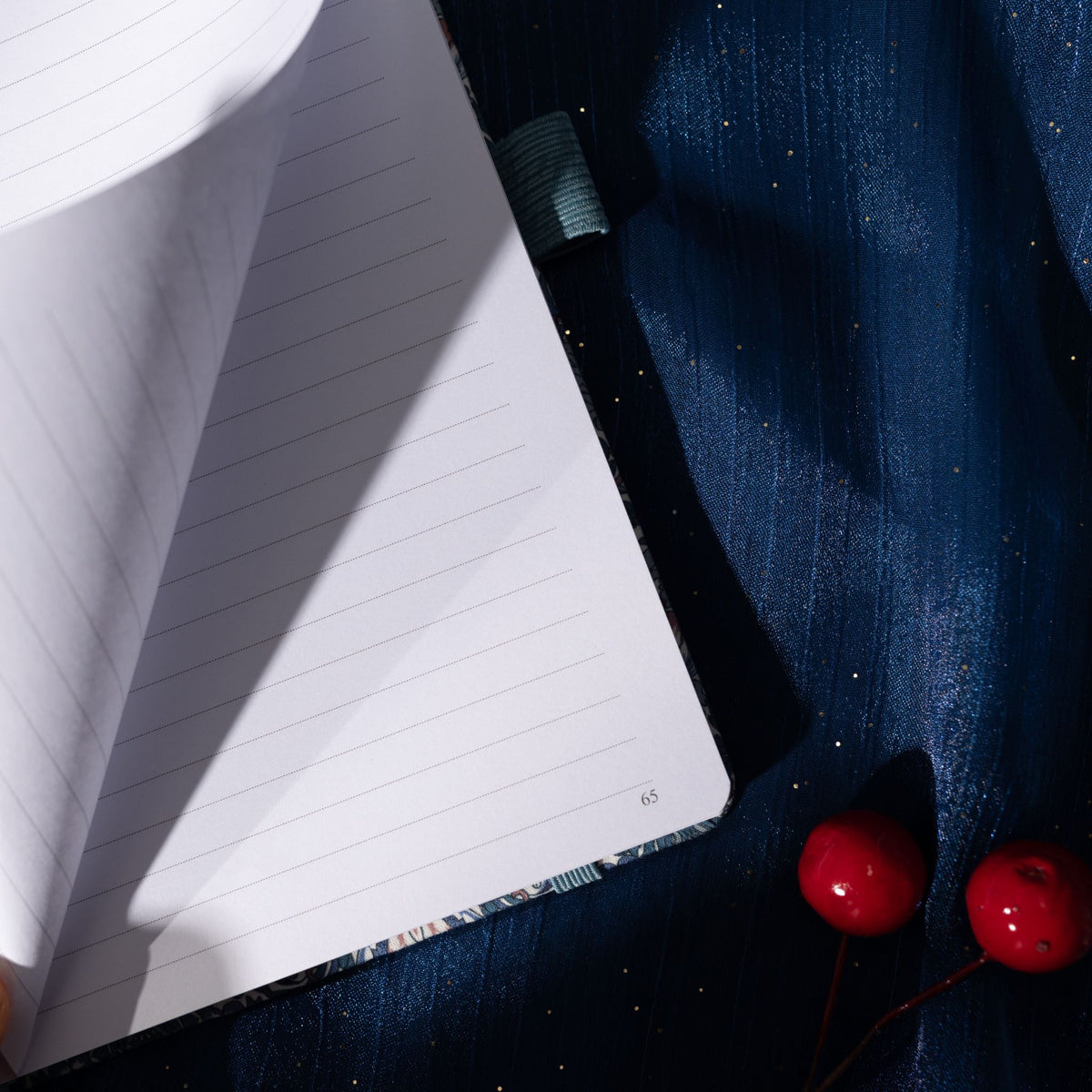 Close-up of a page being turned in the blue floral fabric notebook, revealing the lined paper interior and corner page number.