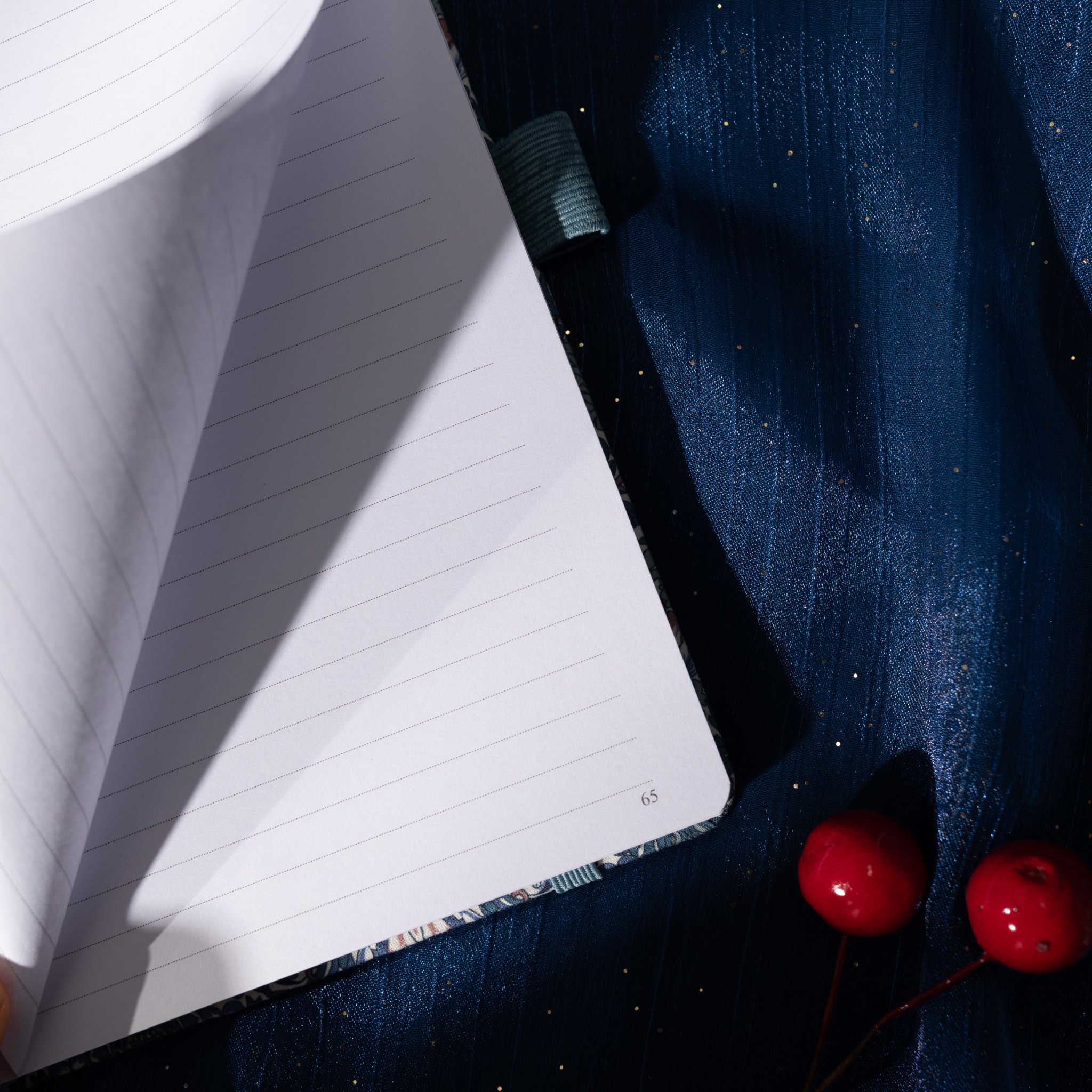 Close-up of a page being turned in the blue floral fabric notebook, revealing the lined paper interior and corner page number.