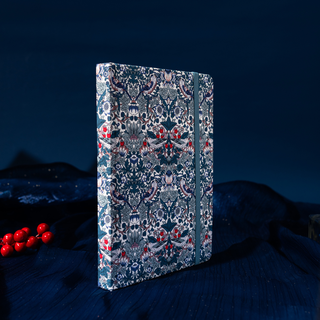 Deep blue floral fabric notebook standing upright on dark blue textured fabric, surrounded by red berries.