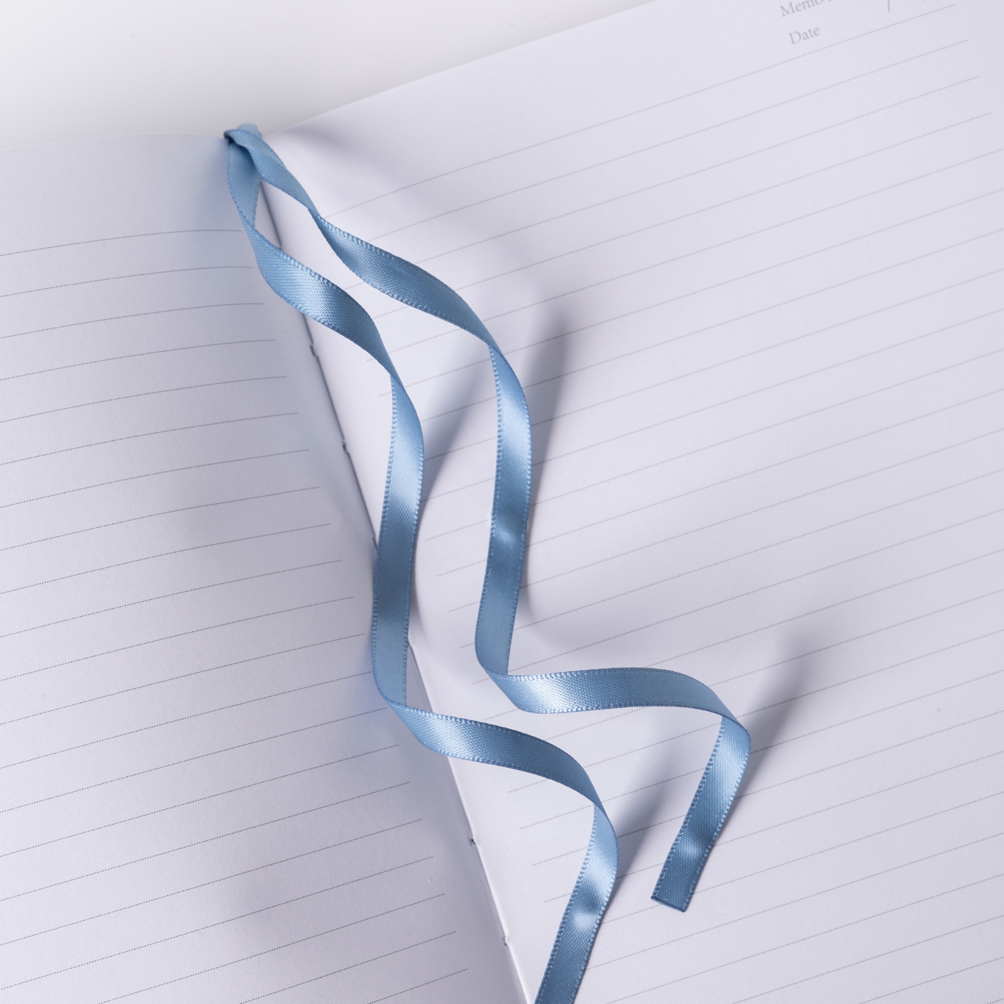 Light blue satin ribbon bookmark resting on the open lined pages of the blue floral notebook, styled on dark blue fabric.