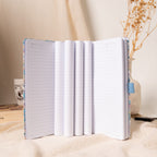 Open lilac and blue floral fabric notebook standing vertically, displaying multiple layered lined pages, a lay-flat binding, and Memo No. and Date headers, styled with a coffee mug and dried flowers on a cream fabric surface.
