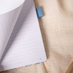 Close-up of a page being turned in the lilac and blue floral notebook, revealing a smooth lined page and corner page number.