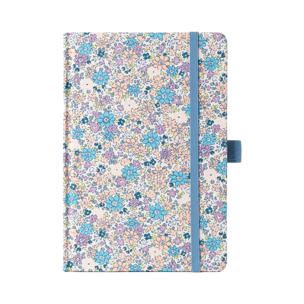 A5 lilac and blue ditsy floral fabric notebook standing upright on a white background, featuring a dense pattern of small pastel purple, blue, and peach blossoms, finished with a matching muted blue elastic closure.