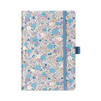 A5 lilac and blue ditsy floral fabric notebook standing upright on a white background, featuring a dense pattern of small pastel purple, blue, and peach blossoms, finished with a matching muted blue elastic closure.