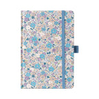 A5 lilac and blue ditsy floral fabric notebook standing upright on a white background, featuring a dense pattern of small pastel purple, blue, and peach blossoms, finished with a matching muted blue elastic closure.