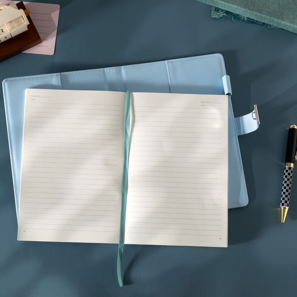 Top-down view of the open light blue floral journal laid flat, showing the lined paper interior, blue ribbon, and lock strap.