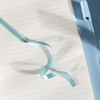 Close-up of the open lined paper interior with a light blue satin ribbon bookmark and a patterned pen.