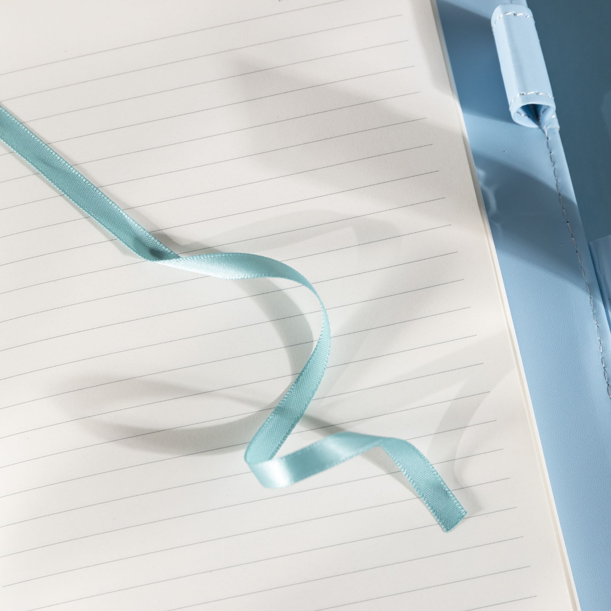 Close-up of the open lined paper interior with a light blue satin ribbon bookmark and a patterned pen.