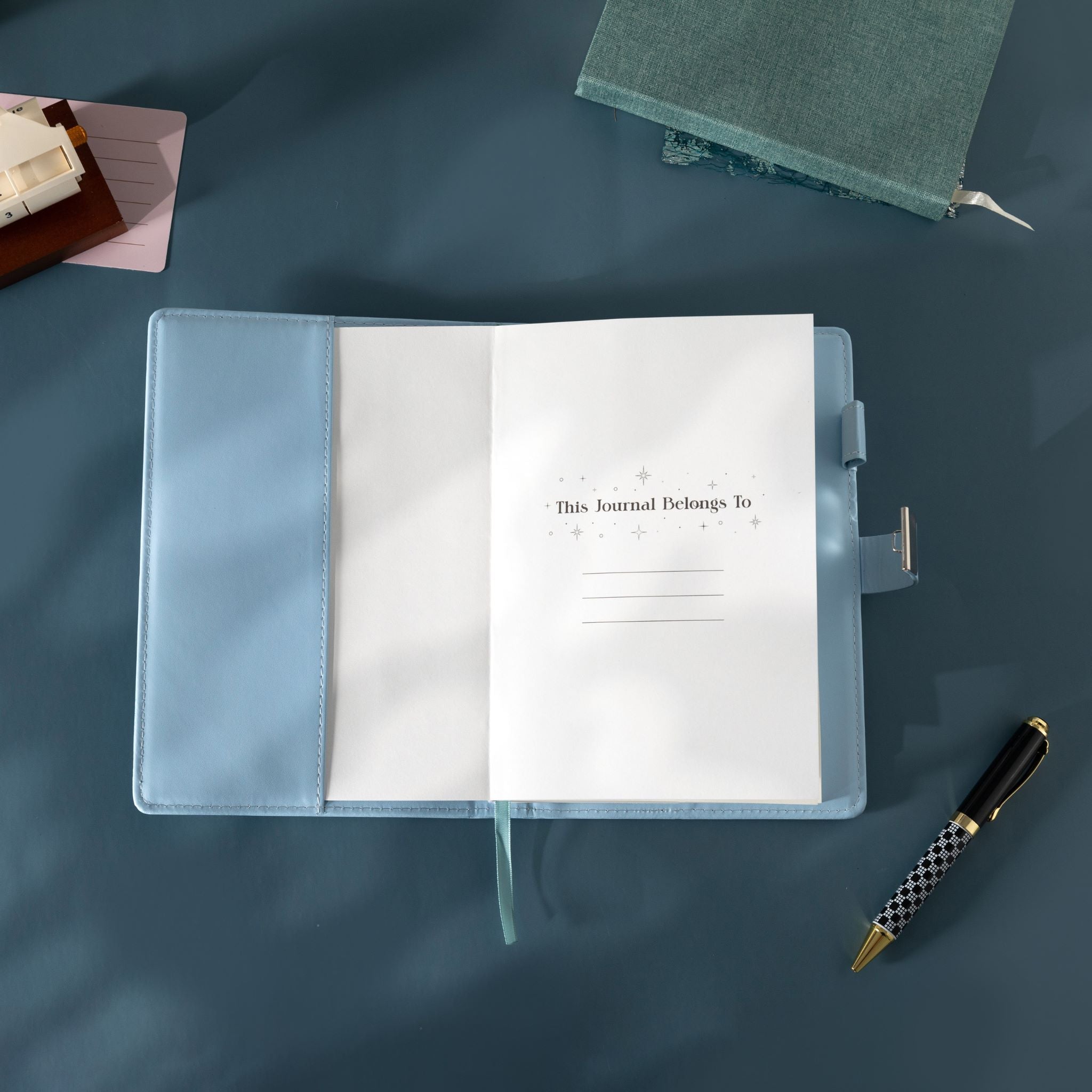 Open light blue vegan leather notebook showing the "This Journal Belongs To" ownership page, laid flat with a matching blue ribbon.