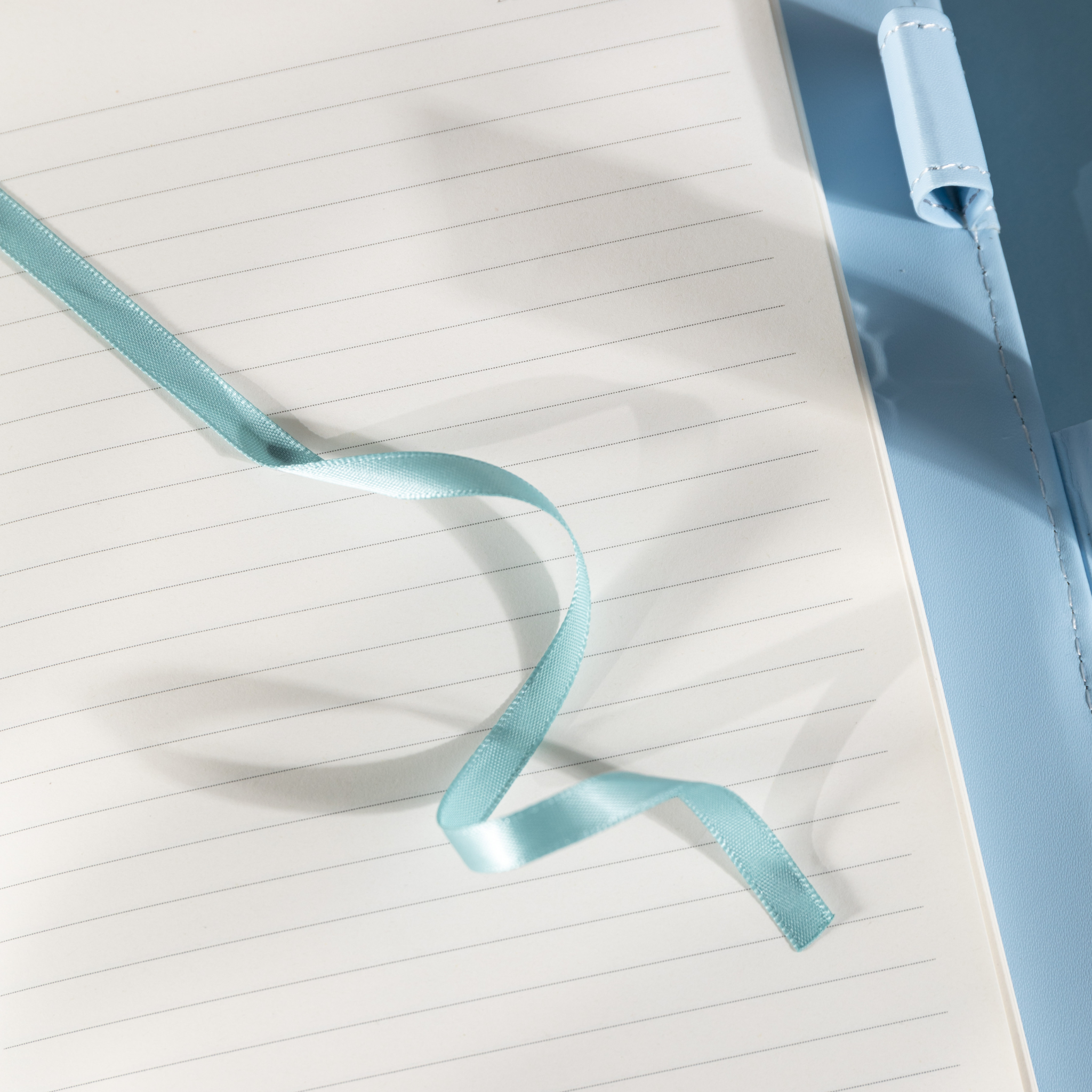 Close-up of the open lined paper interior with a light blue satin ribbon bookmark and a patterned pen.