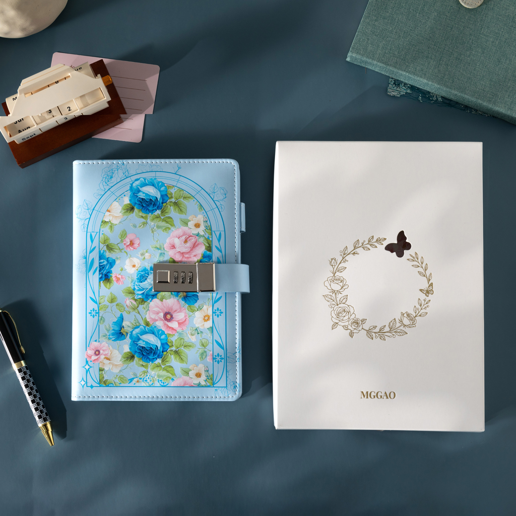 Light blue floral vegan leather notebook with lock placed next to its white gift box with a gold foil wreath logo.