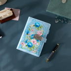 Top-down view of the light blue floral vegan leather notebook laid flat on a dark surface, showcasing the botanical arch design and metal lock.