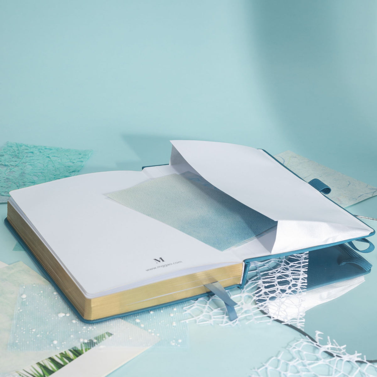 Inner back pocket of the blue vegan leather notebook holding a white card, with elegant gold gilded edges visible at the bottom.