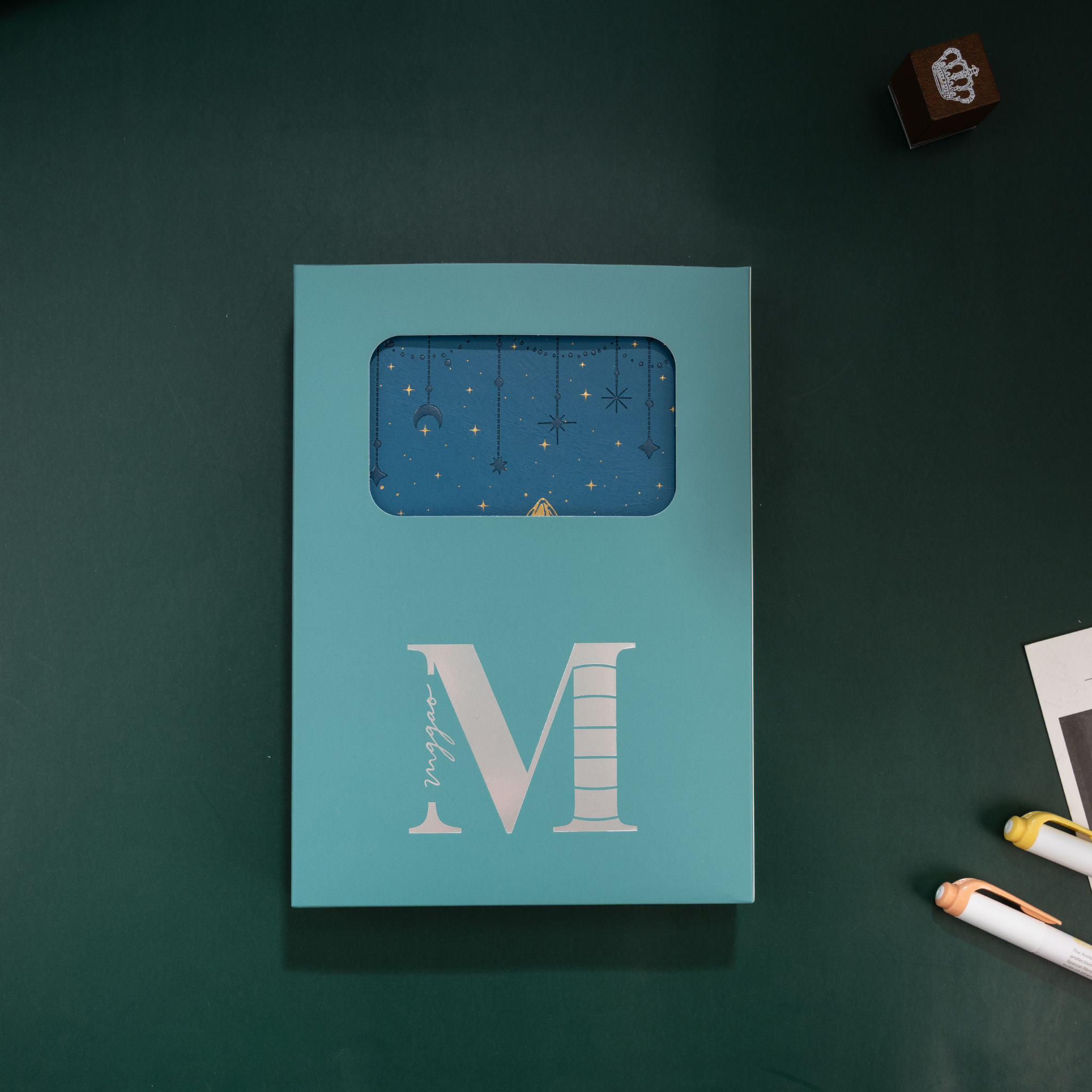 Light blue window-cut gift box featuring a white "M" logo, displaying the deep blue mountain vegan leather notebook inside.
