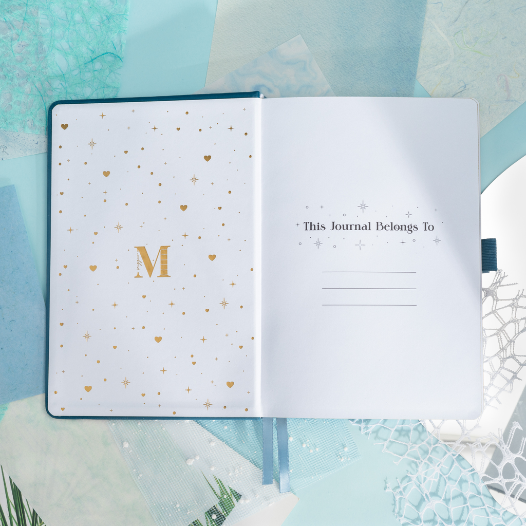 Inside opening page of the deep blue mountain journal featuring a gold foil "M" logo and "This Journal Belongs To" ownership section.