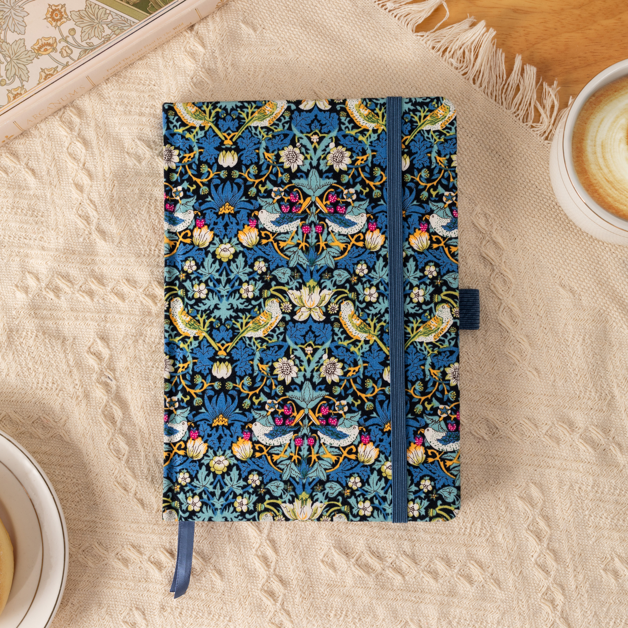 Flat lay of the blue bird and floral fabric notebook on a cream textured blanket, surrounded by soft natural decor.