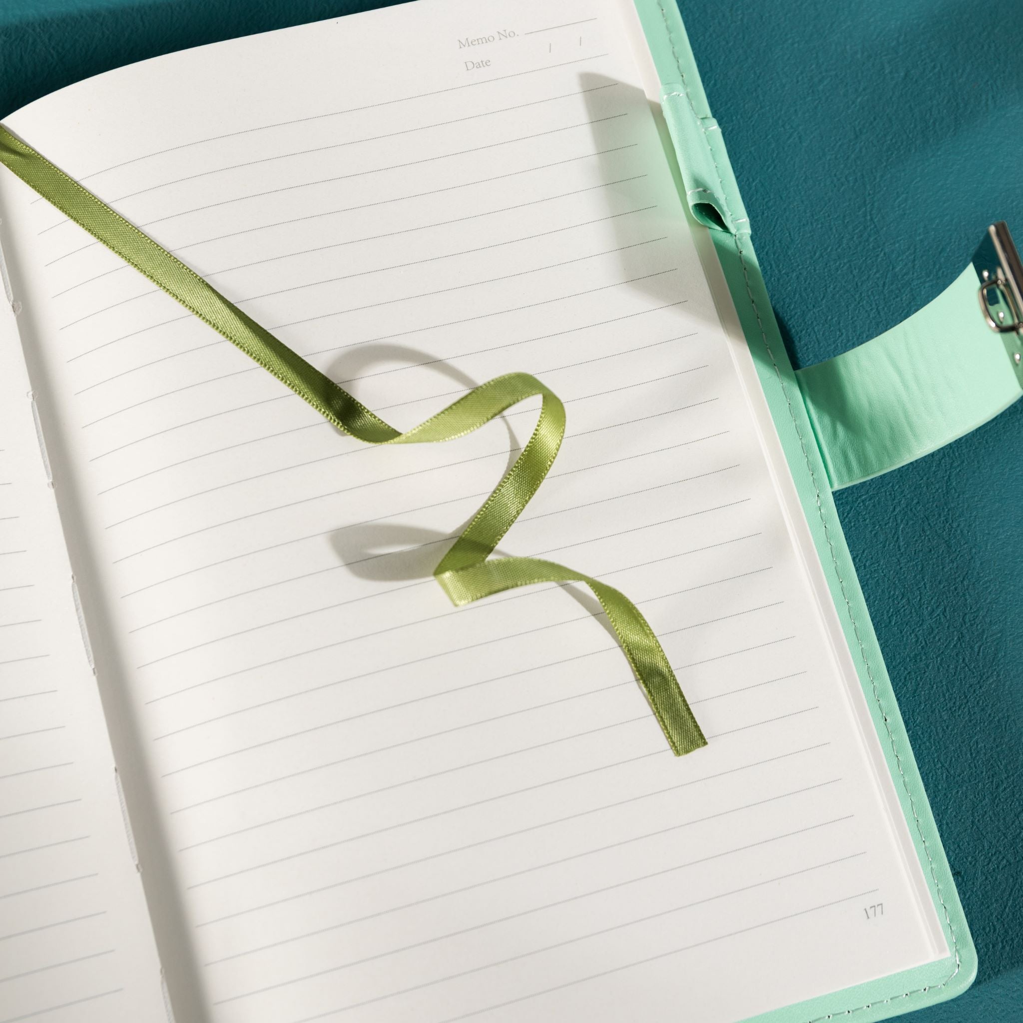 Close-up of the open lined paper interior with a green satin ribbon bookmark and a patterned pen.