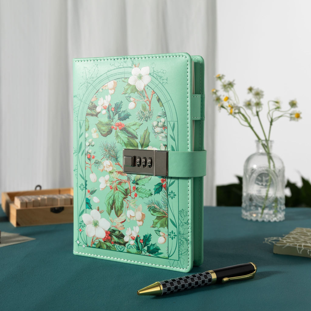 Green floral vegan leather journal with a metal password lock, standing upright on a dark green desk with a pen and dried flowers.